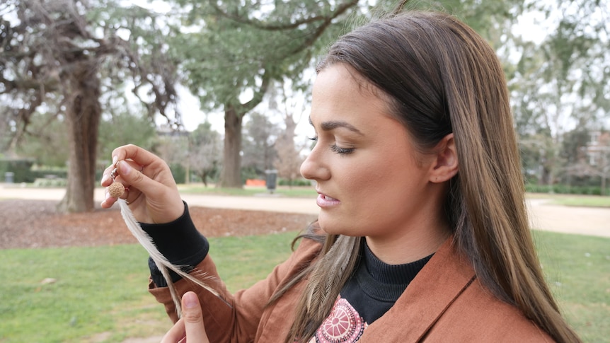 A girl holding a Quandong and Emu feather earring.
