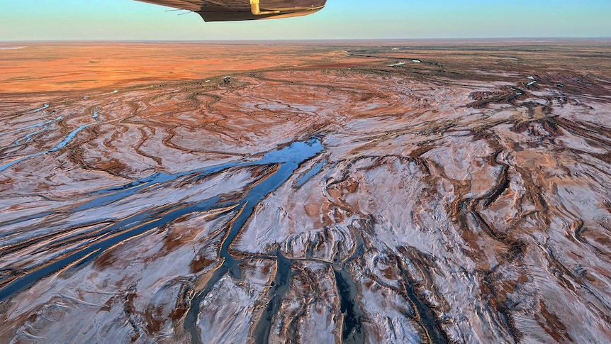 Aerial shots of a dry red landscape with blue water flowing through it.