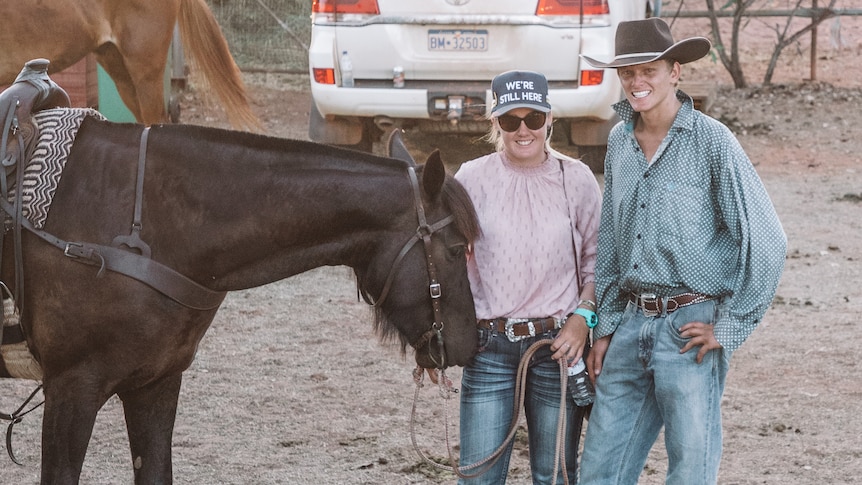 A young man and woman stand smiling as they hold the reins of a horse.