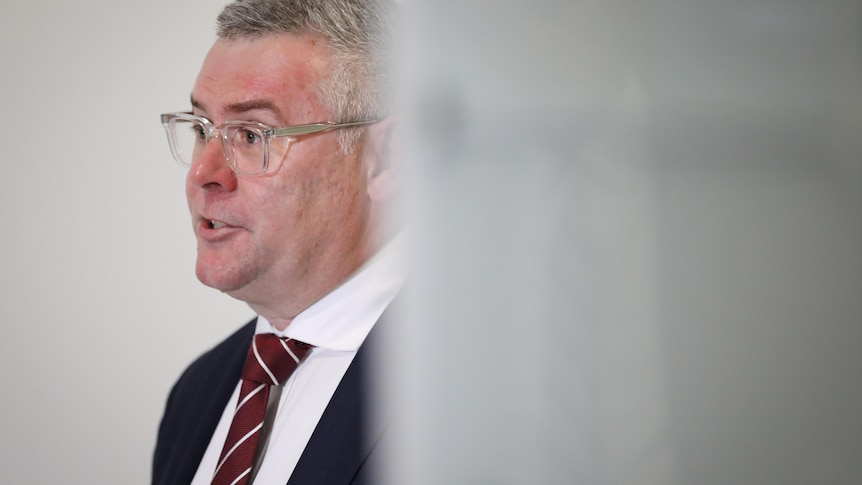 A grey-haired, bespectacled man in a dark suit.