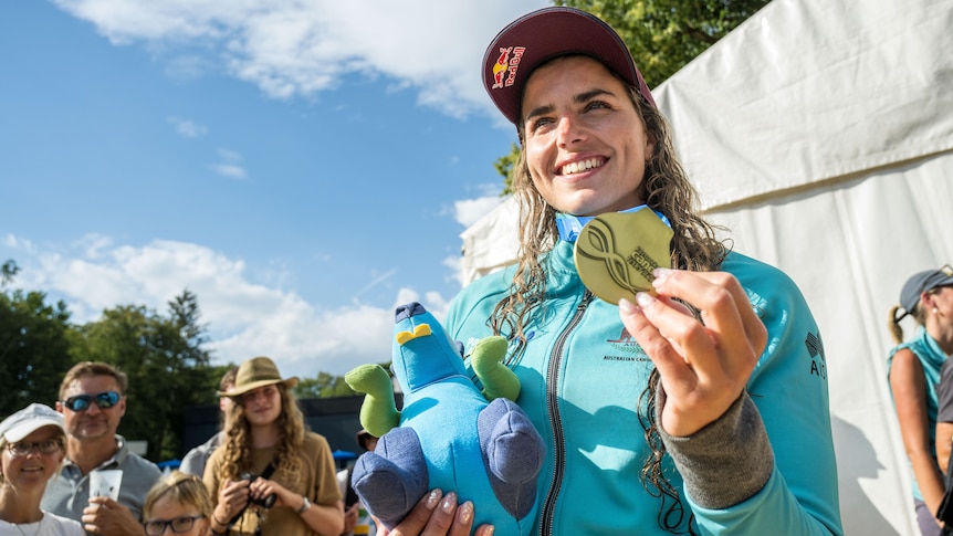 Jess Fox poses for a photo with her world championship gold medal, a hat and plushie