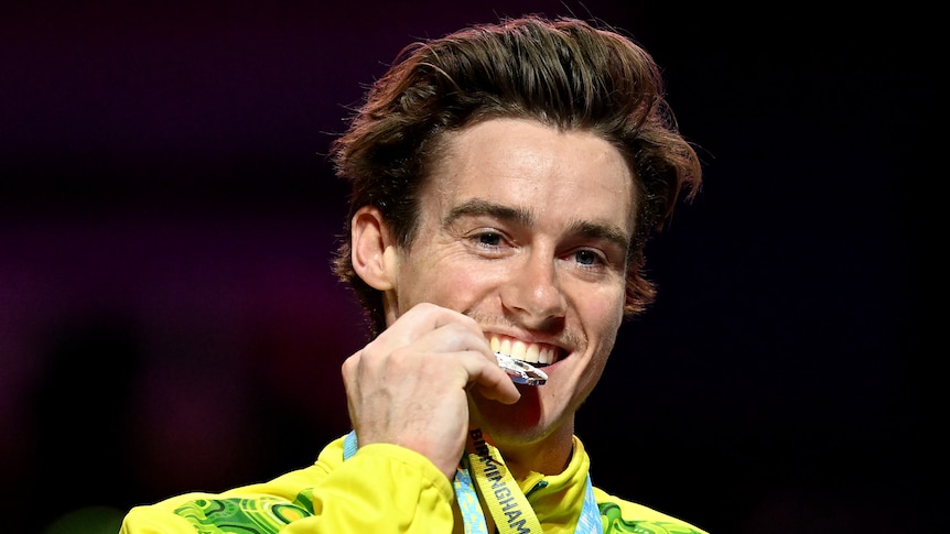 An Australian gymnast smiles as he bites into his silver medal after his event at the Commonwealth Games.
