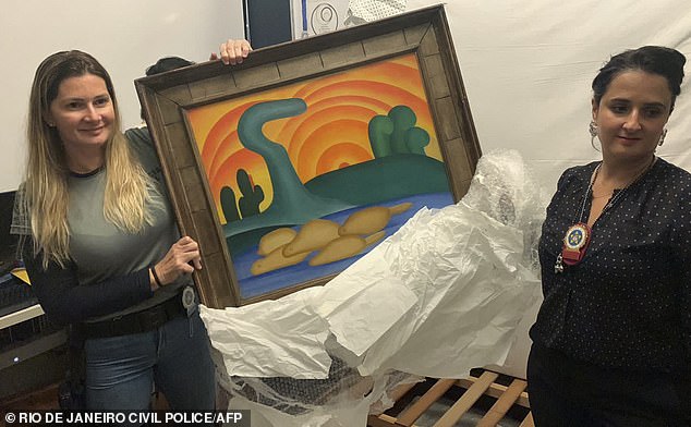 Police officers pose with Sol Poente by Tarsila do Amaral, which is worth £48million alone.  Its owner, Genevieve Boghici, 82, was 'swindled out of the painting' by her daughter de ella and psychics