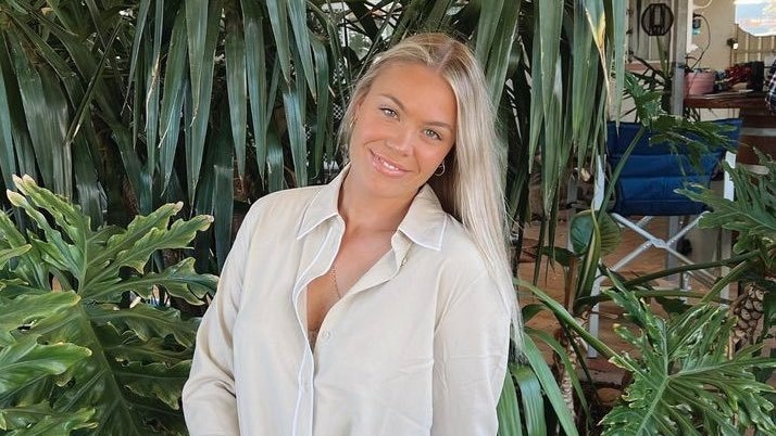 A blonde woman wearing a white blouse and blue jeans sitting in a garden