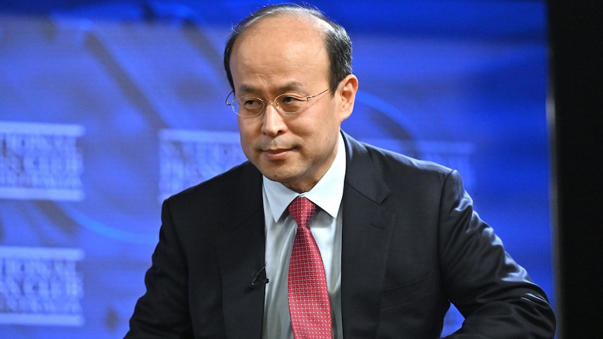 China's Ambassador to Australia Xiao Qian in a suit and glasses.