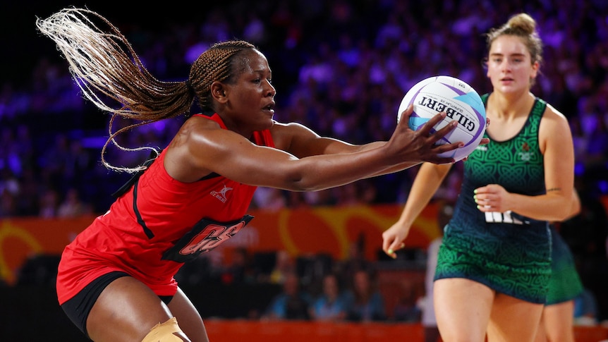 A Malawi netballer's hair flies behind her as she reaches out to grab the ball ahead of a Northern Ireland opponent.