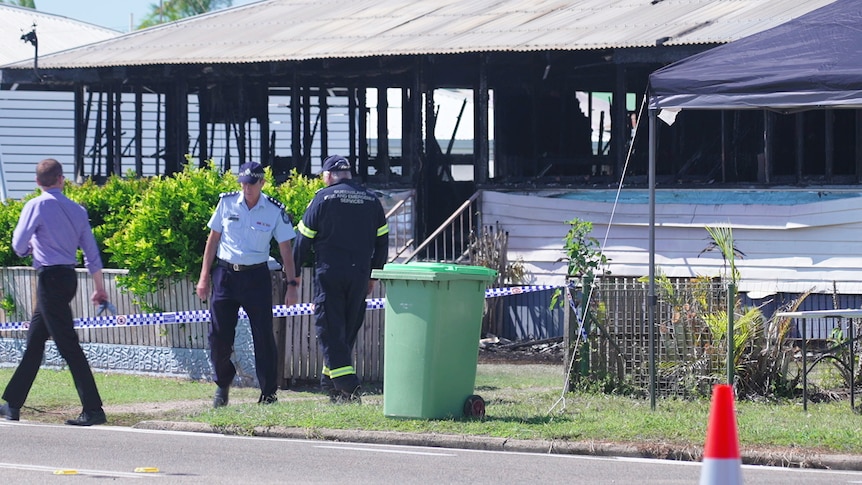 A police officer and fire fighter stand outside a burnt-out home surrounded by police tape