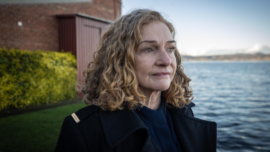 A woman looks seriously to the side of the camera, gazing out over water.