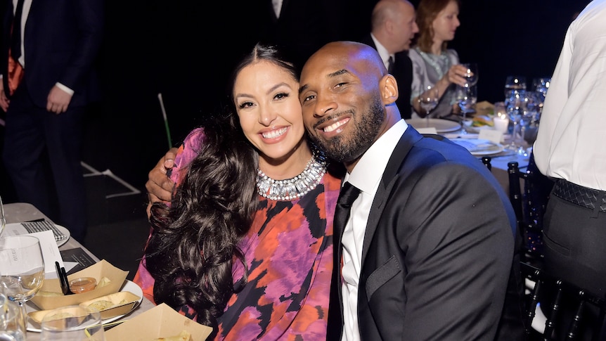 vanessa and kobe bryant sitting at a dining table smiling, kobe has his arm around vanessa and their faces are close together