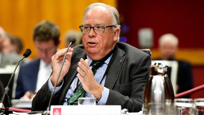 a man with hands lifted sitting behind a desk with his hands lifted