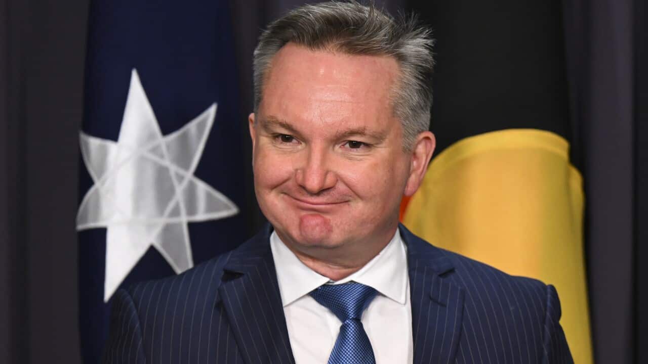 Climate Minister Chris Bowen smiling in front of Australian and Aboriginal flags.