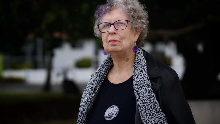 A woman wearing a black top with a scarf and black-framed glasses.