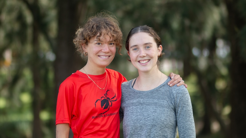 Two young women with their arms around each other smile at the camera