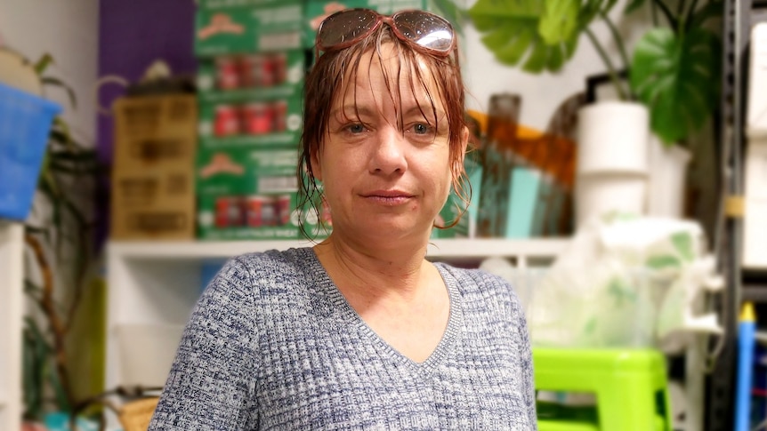 A woman stands in front of a stockpile of food and essentials at a homeless shelter