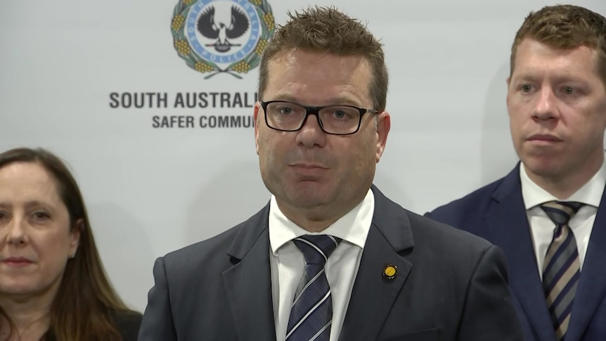 Detective standing in suit with woman and man beside him