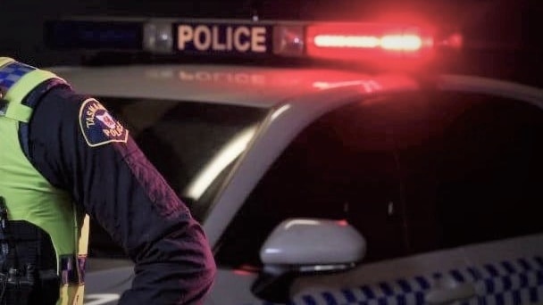 Flashing lights on Tasmania Police car with unidentified officer nearby.