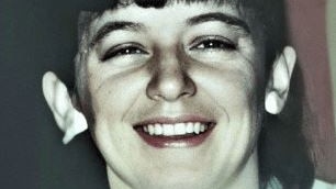 Old, close-up photo of a smiling woman with dark, shoulder-length hair.