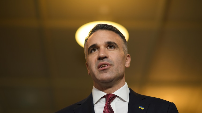 A man in a suit speaking with a round light shining above his head.