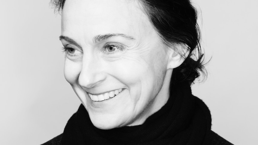 A black and white image of a middle-aged woman smiling with eyes cast down looking to the left