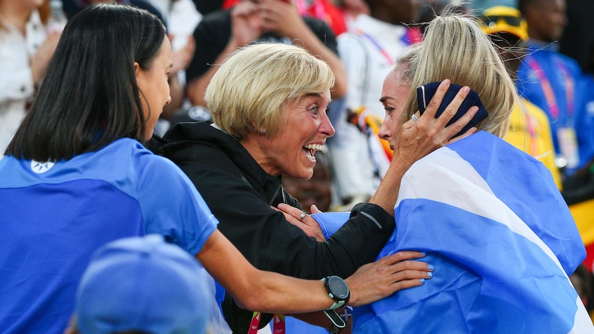 A woman wears a beaming smile as she looks at a female athlete who is wrapped in a Scottish flag after a race.