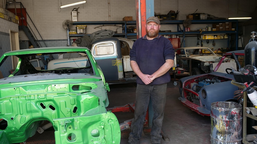 A man in a cap stands in a garage full of cars