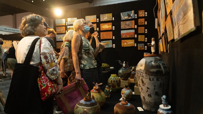 A group of women looks at paintings and pottery on display inside an art gallery.