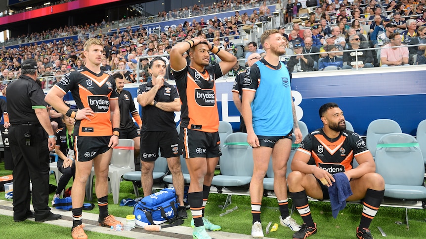 A group of Rugby players in orange and black kits look on with anguish from sideline of packed stadium