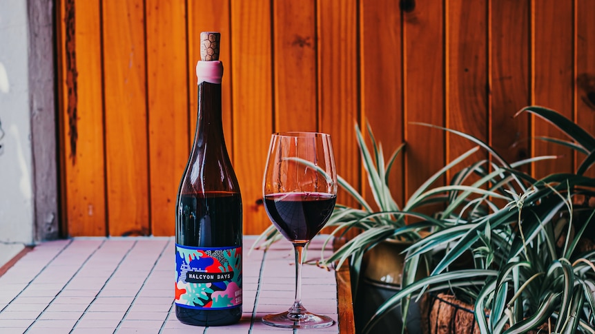 A bottle of red wine with a colourful label and a cork sticking out.