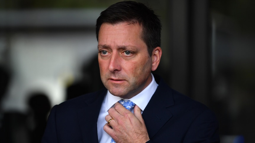 A profile shot of a man wearing a suit holding onto his tie knot.